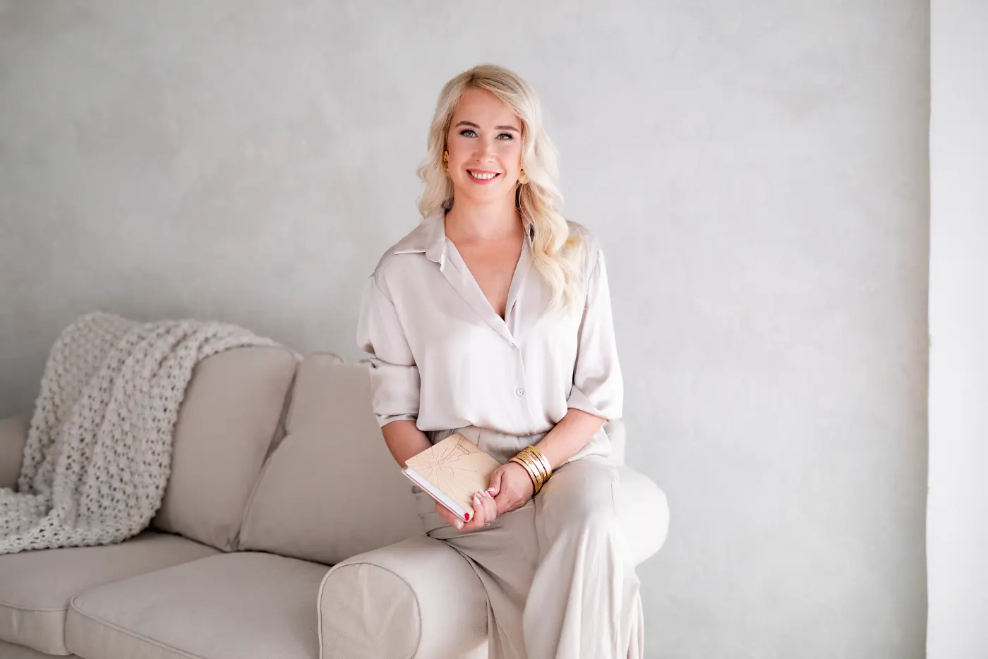 Svetlana Ambre дружелюбно улыбается, сидя на диване с тетрадью в руках