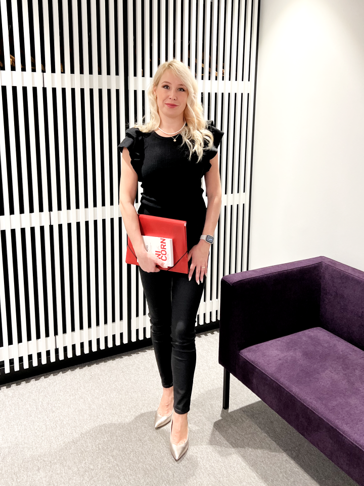 Svetlana Ambre стоит с папкой и книгой в руках в деловой обстановке рядом с диваном