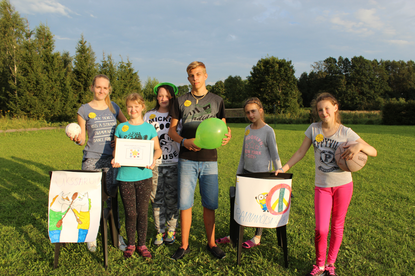 Шестеро детей стоят с нарисованными плакатами в руках на зеленом газоне на фоне леса